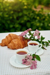 Two cup black tea with flowers and fresh croissants on the table against white background. Flat lay, spring breakfast conceptual composition