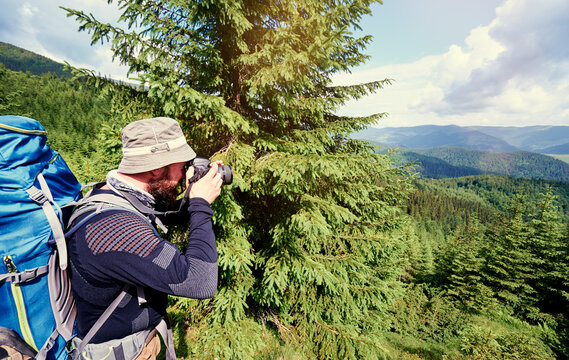 Traveling and photography. Young man with camera and backpack taking picture in mountains forest.
