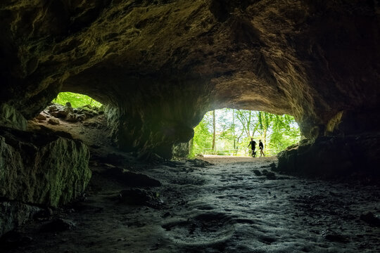 Inside of Feldhof cave looking outside into the green forest with silhouette of people outside, Balve, Sauerland, Germany