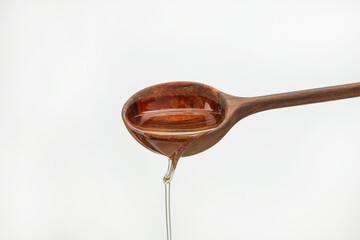 Stream of oil pours  from a wooden spoon on a white background. Shallow depth of field