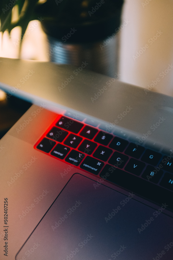 Poster vertical shot of a half-opened laptop keyboard with under the red light from the screen