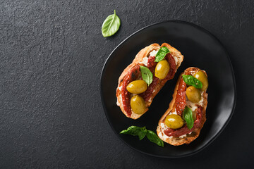 Bruschetta with sun dried tomatoes. Toast or sandwich with ricotta, sun dried tomatoes and Provence herbs with basil servered on black plate on black background table. Top view banner menu recipe.