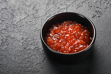 Red salmon caviar. Delicious red caviar in black bowl on black dark concrete background. Top view with copy space. Flat lay. Mock up.