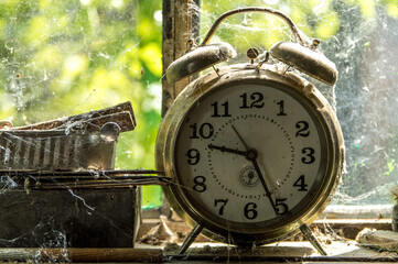 Old dusty analog clock covered with cobwebs in a window of a workshop