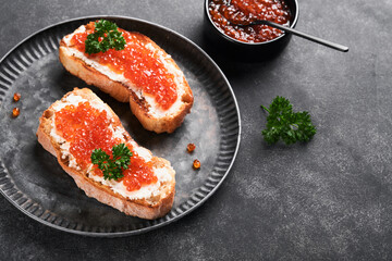 Two dandwiches with red caviar. Salmon red caviar in bowl and sandwiches server on old iron plate on old black table background. Top view. Copy space.