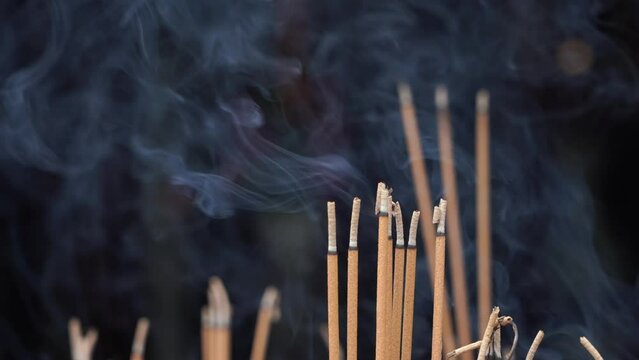 Close-up of incense sticks burning with smoke and a praying man in buddhist temple of Danang city, Vietnam