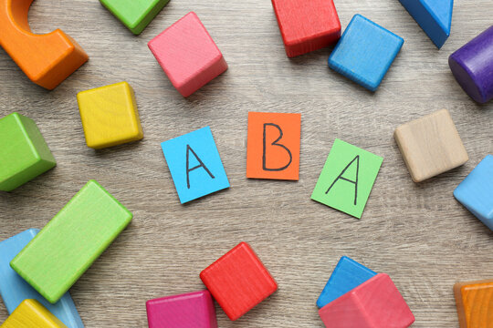 Colorful building blocks and cards with abbreviation ABA on wooden table, flat lay