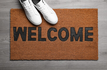 New clean mat with word WELCOME and shoes on floor, top view - obrazy, fototapety, plakaty
