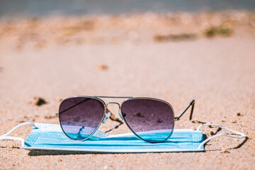 sunglasses on the beach and medical mask, concept of summer vacations with protection