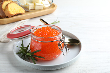 Glass jar of delicious red caviar served with rosemary on white wooden table