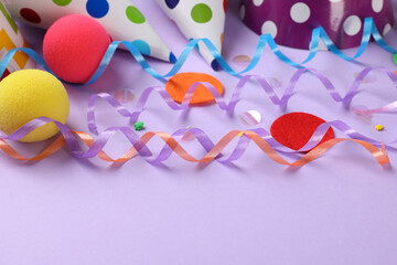 Colorful serpentine streamers and other party accessories on violet background, closeup