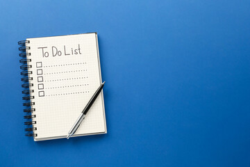 Notepad with unfilled To Do list and pen on blue background, top view. Space for text