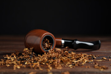 Smoking pipe and dry tobacco on wooden table against dark background. Space for text