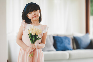 Happy smiling little Asian girl holding bouquet of flowers in living room