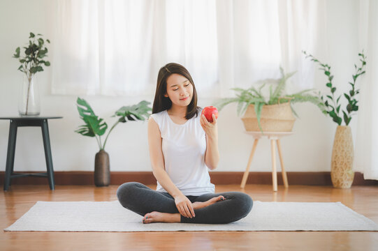 Smiling Asian Woman Eating Red Apple Before Doing Workout Exercise At Home. Healthy Lifestyle