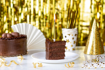 Birthday party background. Chocolate cake with golden candles, birthday hat and accessories on shine bokeh golden background.