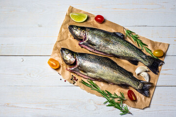Raw fish, trout with on craft paper with ingredients for cooking. Fish, pepper, garlics, tomatoes, lemon and rosemary on white wooden table. Healthy food and dieting concept flat lay, top view image