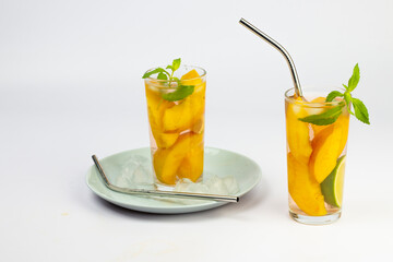 Refreshing summer drink. Peach juice or tea with peach slice, ice cube, straws and mint on white background.