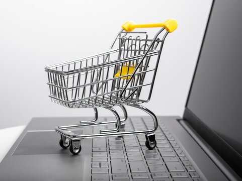 Supermarket trolley at laptop keyboard. Online shopping and electronic commerce concept. Buying goods via Internet. High quality photo