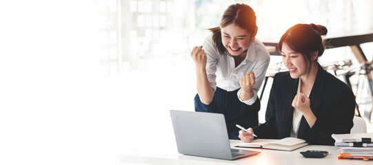 Two Elegant businesswoman sitting in office with laptop. Excited asian business people raising hands to congratulate while working on laptop in office. - obrazy, fototapety, plakaty