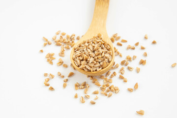 Wooden spoon with whole grain wheat groasts on a white isolated background.