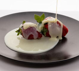 strawberry dripping condensed milk on a black plate and white background