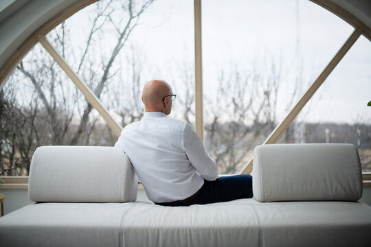 Rear view of thinking man relaxing on the sofa at home while looking out the window