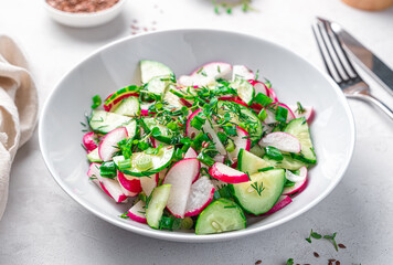 Fresh vegetable salad with radish, cucumber and fresh herbs on a light gray background. Dietary, healthy salad. Side view, close-up.