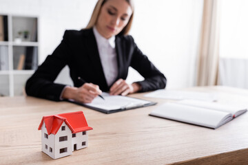 selective focus of house model and blurred notary signing contract on blurred background.