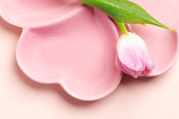 Spring table setting - empty pink plate in form of heart and pink tulip close up on pastel pink.