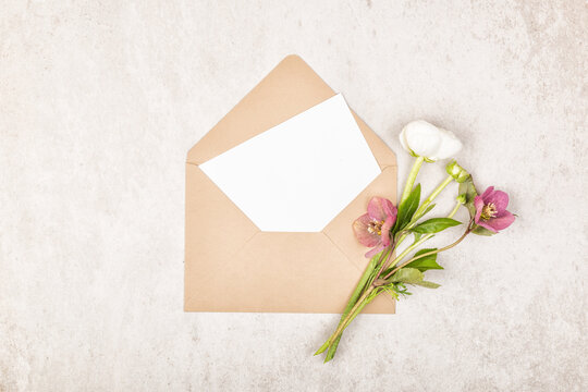 Beige craft envelope with blank white note card and bouquet of purple Hellebore flowers. Vintage or wedding, invitation, save the date, greetings card. Top view and flat lay with copy space - Powered by Adobe