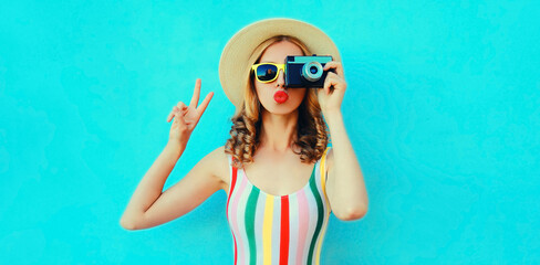 Summer portrait of happy stylish young woman photographer with film camera blowing her lips with...