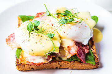 Eggs benedict on crispy toast with bacon and traditional hollandaise sauce. Delicious breakfast concept.