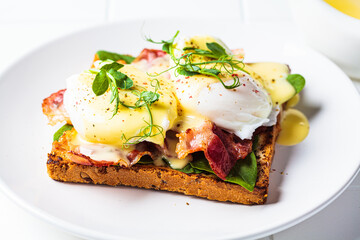 Eggs benedict on crispy toast with bacon and traditional hollandaise sauce. Delicious breakfast concept.