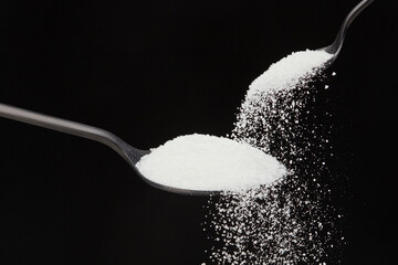 Falling natural sugar from a small spoon into a big black spoon on a black background. Shallow...