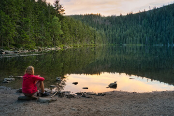 A woman sitting on the bank of beautiful Devil's Lake in the Bohemian Forest, Czech Republic