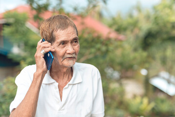 An 70 year old asian man reconnecting with his friend by conversing over the phone. Outdoor scene.