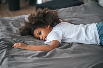 A curly-haird girl feeling tired after playing and laying on bed