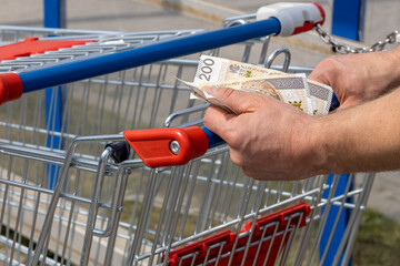 Shopping cart in a supermarket and Polish zloty money, held in hand, Concept of inflation, Rising...