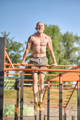 A gray-haired mature man having a workout on the open sports ground