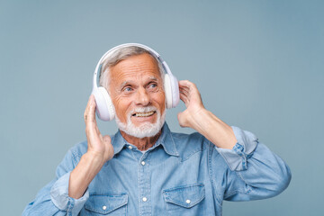 Studio portrait of relaxed cheerful man wearing and holding wireless headphones isolated on blue...
