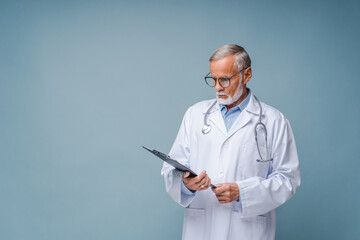 Mature physician therapist reading treatment plan, prescription. Senior doctor in white medical...