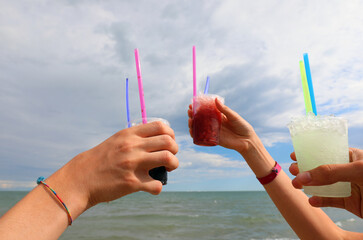 hands toasting with grenadine and iced glucose syrup by the sea with glasses