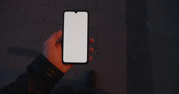 POV male hand holding smartphone with blank empty screen at night street