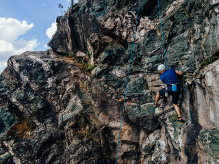 Focused man, using strength, climbing on the side of a rock.