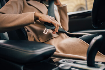 Female dressed in a coat, putting on a seatbelt, ready to drive.
