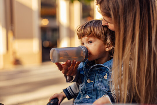 Photo of a cute male toddler, drinking water with mom's help.
