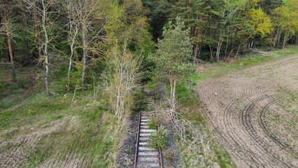 Old abandoned, overgrown railway track. Unused railway going through the spring field into a tiny forest