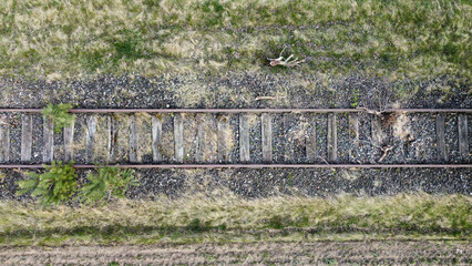 Old abandoned, overgrown railway track. Unused railway going through the spring field into a tiny forest. Top view, drone