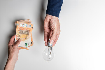 One hand holds light bulb while another delivers bunch of bills